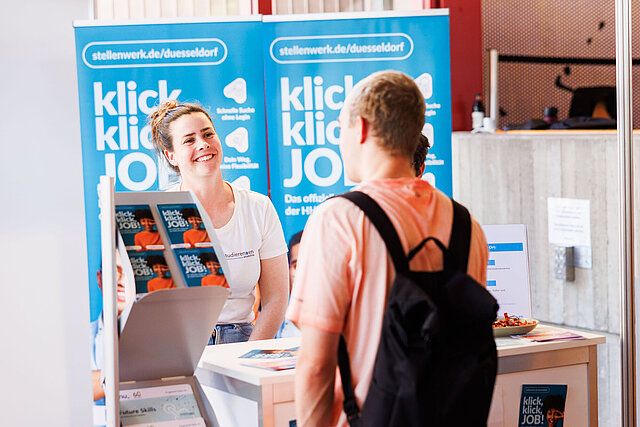 Beratungsszene am Messestand der studierendenakademie