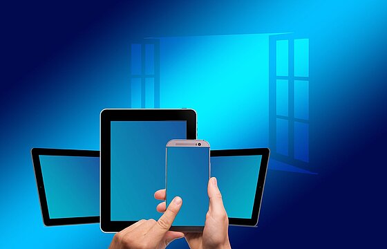 Stilisierte Hände halten ein Smartphone, ein Tablet und weitere Geräte