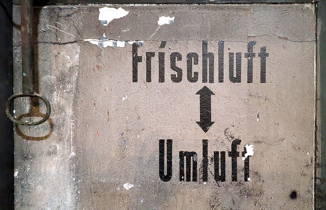 Blick auf eine Wand, auf der zwischen einem Pfeil die Wort Frischluft und Umluft stehen. 