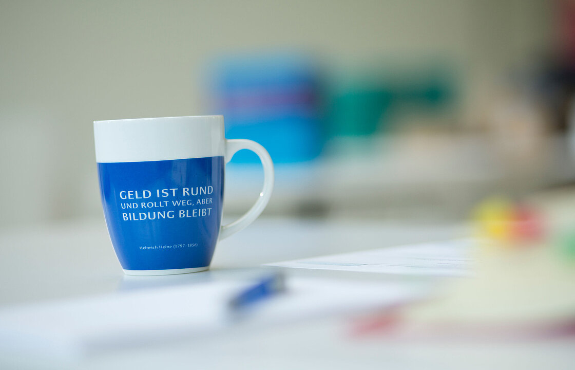 Eine Tasse mit dem Heine-Zitat "Geld ist rund und rollt weg, aber Bildung bleibt."