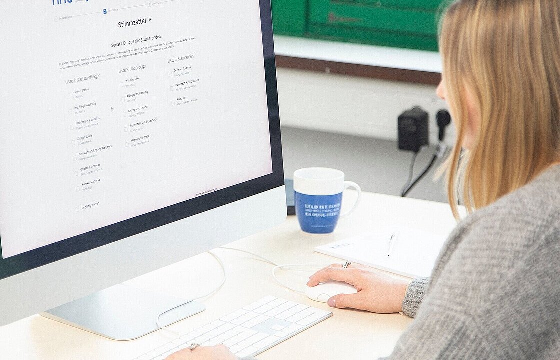 Eine Person sitzt an einem Schreibtisch vor einem PC-Monitor