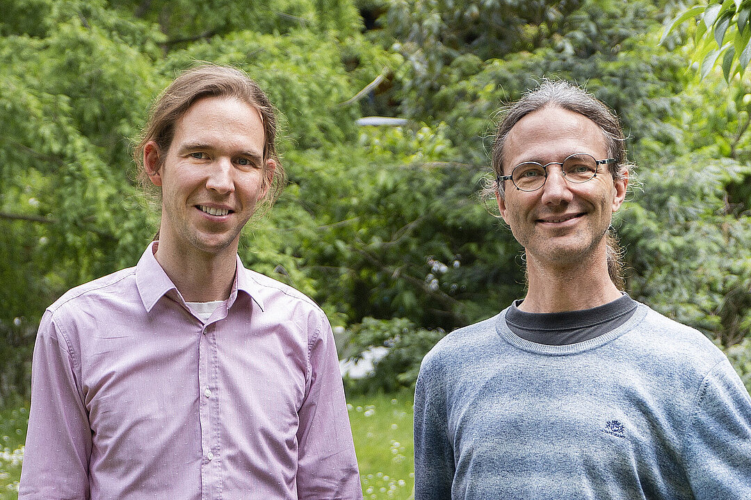 Zwei Personen stehen vor grünem Hintergrund nebeneinander.