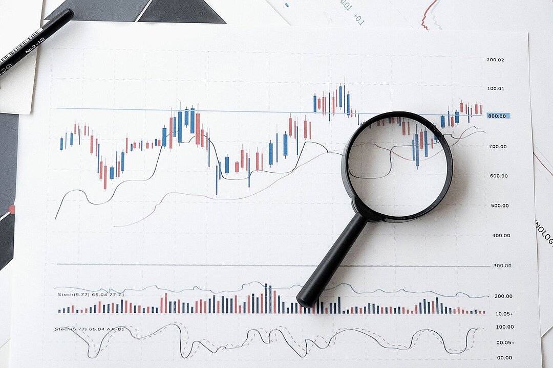 Eine Lupe liegt auf Dokumenten mit grafischen Auswertungen