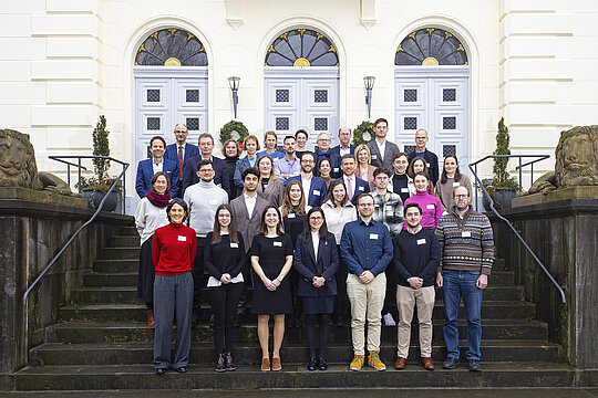Die Teilnehmenden des Retreats, unter ihnen Prof. Lüdde (Sprecher des Clinician Scientist-Programms), Prodekan Prof. Dr. Ertan Mayatepek und Prodekan Prof. Dr. Reifenberger, stehen aufgereiht vor dem Schloss Mickeln auf einer Treppe. Im Hintergrund ist der Haupteingang des Schlosses zu sehen.