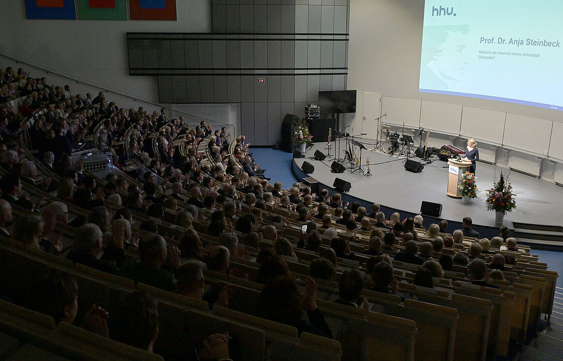 Eine Person in einem voll besetzten Hörsaal hält am Pult vorn eine Rede.