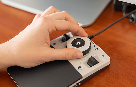 Eine Hand greift nach einem Rädchen an einem digitalen Hilfsmittel, um Webseiten zu vergrößern.