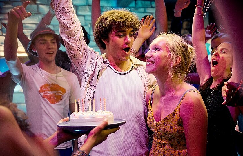 Eine Geburtstagstorte mit Kerzen und mehrere Personen drumherum