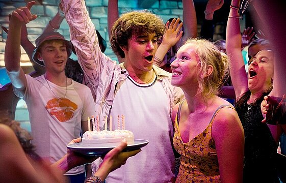 Eine Geburtstagstorte mit Kerzen und mehrere Personen drumherum