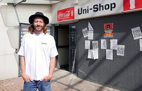 Eine Person mit Hut steht vor dem früheren Uni-Shop der HHU