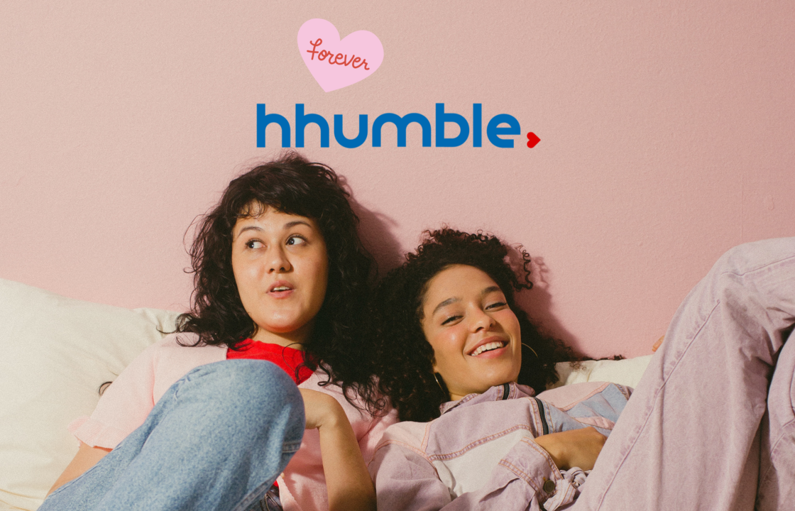 Zwei junge Frauen liegen nebeneinander lachend auf einem Sofa oder Bett. Über ihnen ist das Logo von HHUMble zu sehen, das an das Logo der HHU angelehnt ist. Wiederum darüber steht in einem rosafarbenen Herz "forever".