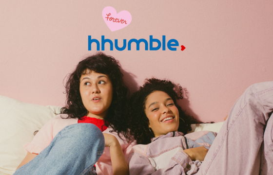 Zwei junge Frauen liegen nebeneinander lachend auf einem Sofa oder Bett. Über ihnen ist das Logo von HHUMble zu sehen, das an das Logo der HHU angelehnt ist. Wiederum darüber steht in einem rosafarbenen Herz "forever".