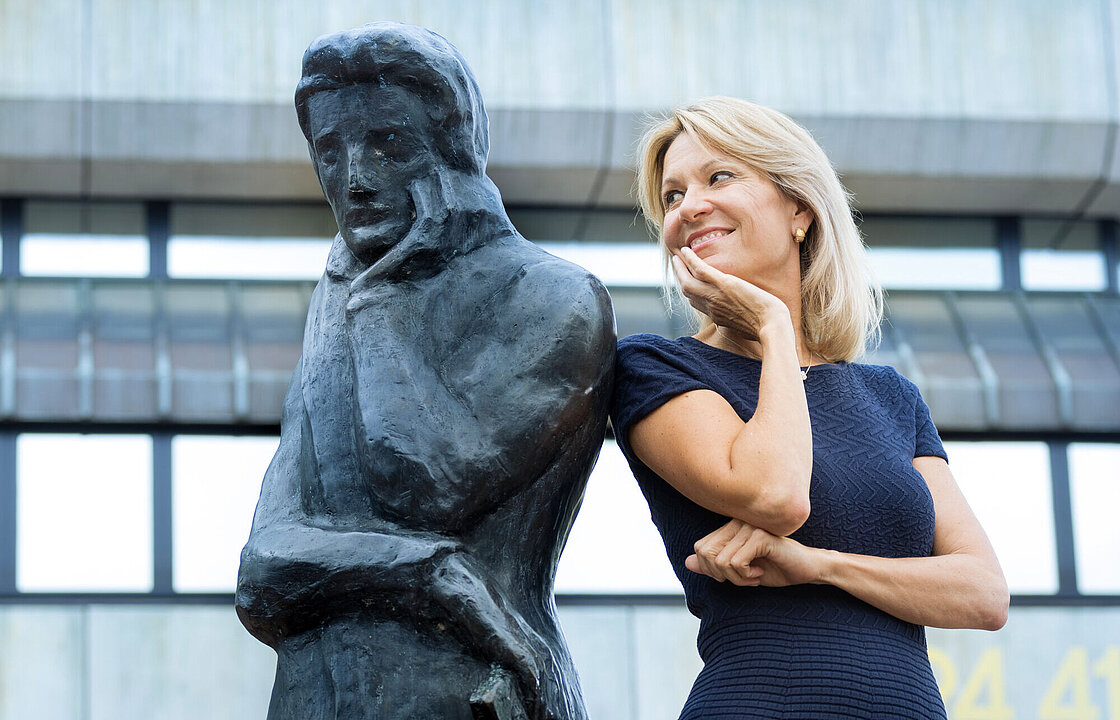Eine Person lehnt an der Heinestatue und schaut sie über ihre Schulter hinweg an.