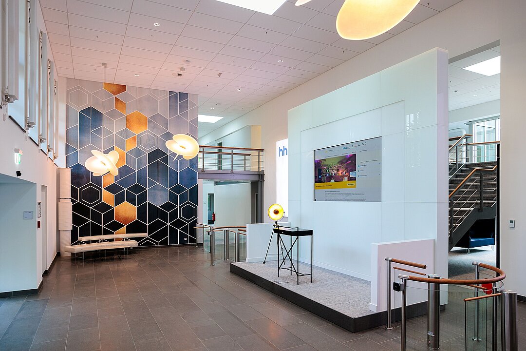 Foyer des ZDM. Modern ausgestattet mit kleiner Bühne mit Bildschirm, auffälliger Beleuchtung und geometrischer Tapete.