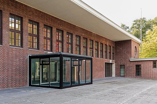 Außenansicht des Gebäudes, roter Backstein-Altbau im Industrial-Stil. Große Fenster, moderner Windfang