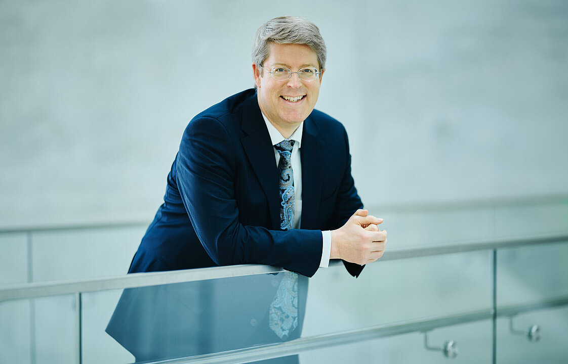 Eine Person lehnt an einer gläsernen Brüstung.