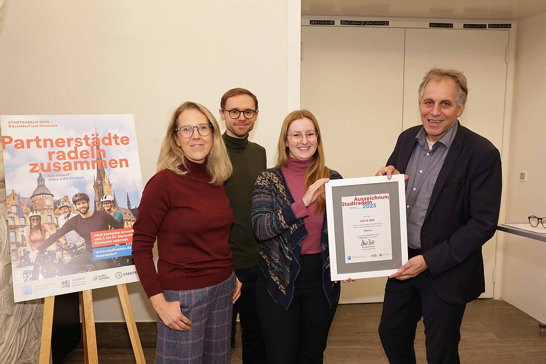 Vier Personen gruppieren sich um eine Urkunde.