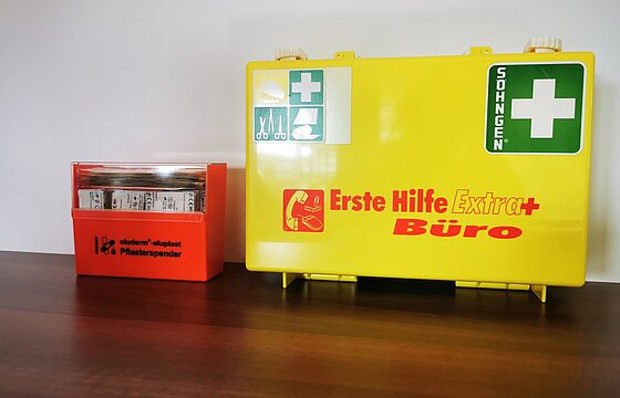 eine orangefarbene Pflasterbox steht neben einem gelben Verbandskasten