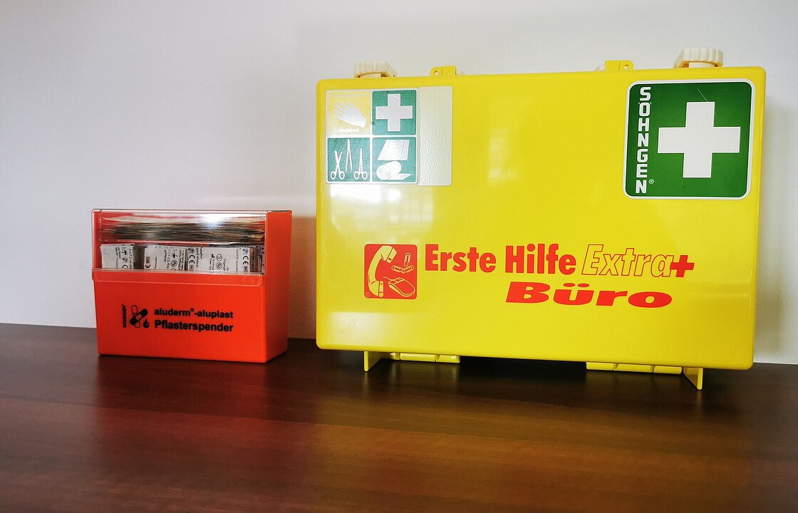 eine orangefarbene Pflasterbox steht neben einem gelben Verbandskasten