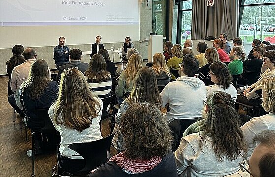 Mehrere Personen sitzen in Reihen vor einer Beamerleinwand