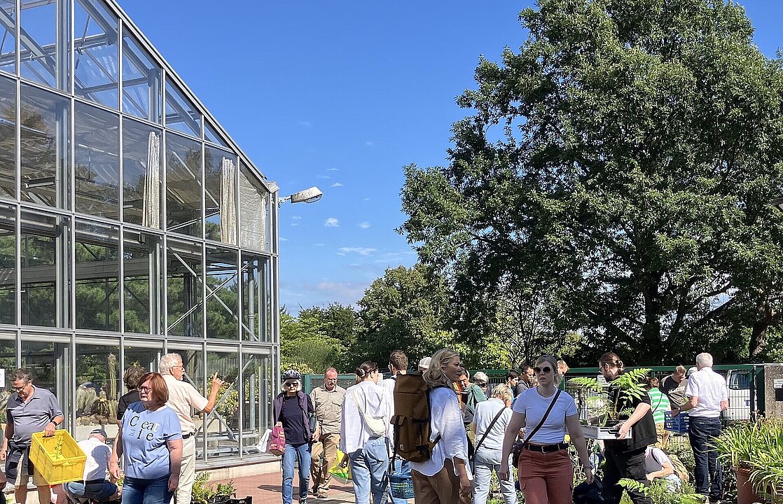 Foto im Gang zwischen den Schaugewächshäusern des Botanischen Gartens, mit vielen Menschen, die die Pflanzenangebote begutachten.