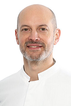 Portraitfoto von Prof. Dr. Roman-Ulrich Müller. Er trägt einen weißen Kittel, Halbglatze und Bart. Der Hintergrund ist weiß.