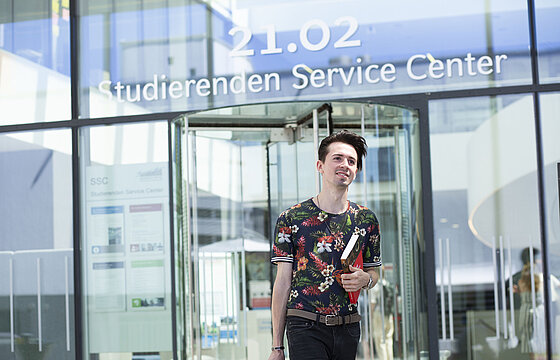Eingang des SSC am Campus mit einer Person im Vordergrund und dem Schriftzug Studierenden Service Center