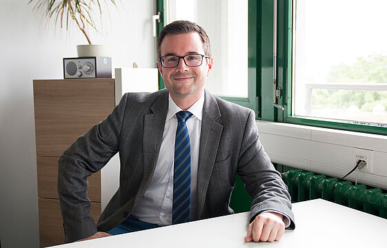 Ein Mensch in Anzug und Krawatte sitzt an einem Schreibtisch