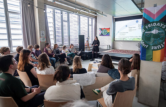 mehrere sitzende Personen hören einer vortragenden Person zu