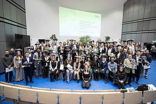 Gruppenbild der anwesenden Promovierten der Mathematisch-Naturwissenschaftlichen Fakultät des Wintersemesters 2025-2026 auf der Bühne von Hörsaal 3A; viele tragen ihren Doktorhut.