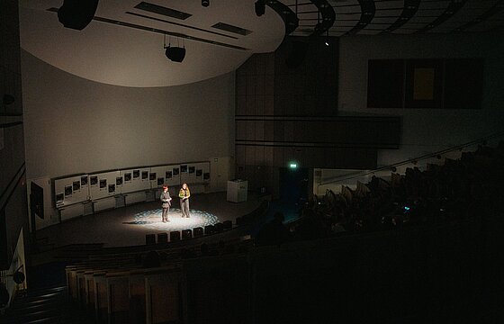 Zwei Personen im Scheinwerferlicht auf der Bühne in Hörsaal 3A beim Filmfest Düsseldorf 2024