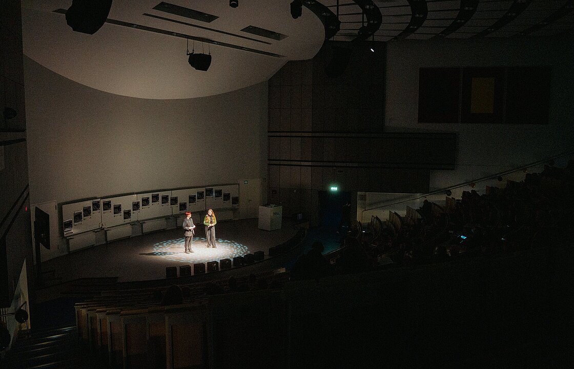 Zwei Personen im Scheinwerferlicht auf der Bühne in Hörsaal 3A beim Filmfest Düsseldorf 2024