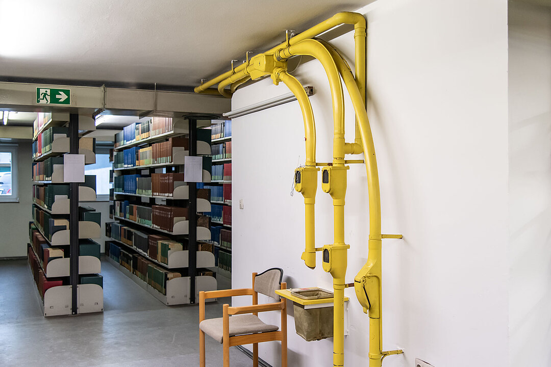 Es ist eine alte Rohrpostanlage bestehend aus gelben Rohren sichtbar. Im Hintergrund sieht man Bücherregale.