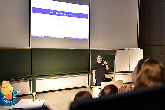 Tobias Löffler im Hörsaal vor Projektion zum Start eines Science Slams.