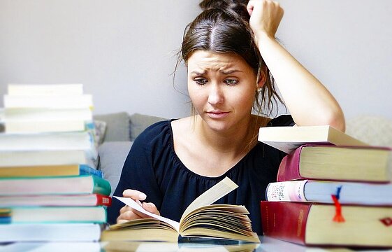 Eine Person sitzt mit gerunzelter Stirn zwischen Bücherstapeln