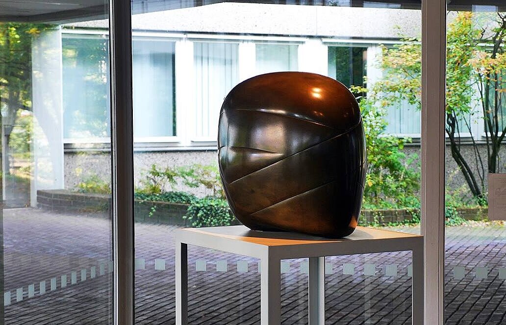 Eine bronzene Plastik auf einer Stele vor Glasfenstern