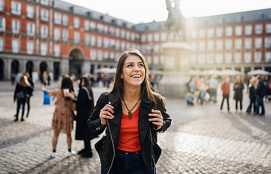 Eine junge Frau steht lächelnd auf einem großen Platz in Madrid