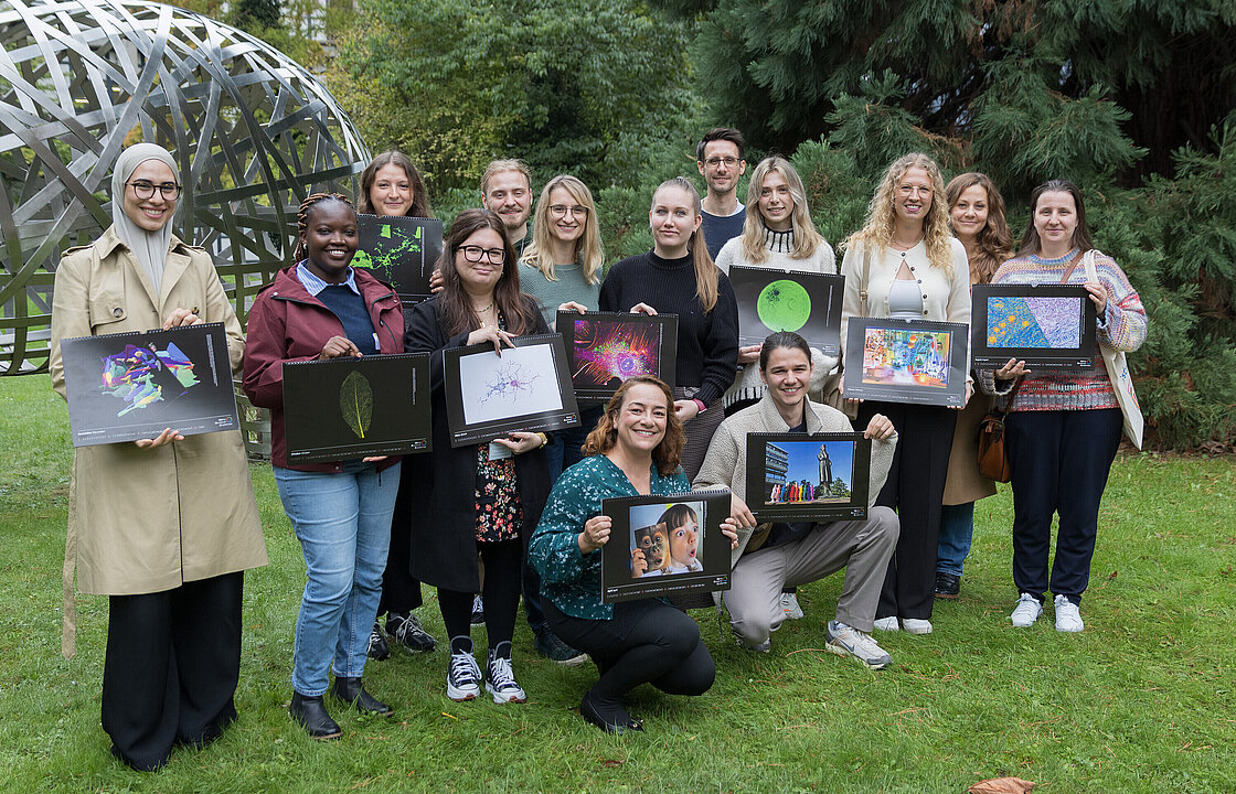 Gruppenbild von 12 Personen mit Kalendern vor dem Kunstwerk zwischen ULB und MNF