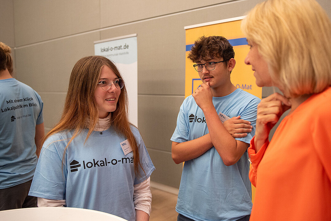 Rektorin Prof. Dr. Anja Steinbeck (rechts) diskutiert mit zwei Personen an einem Stehtisch.