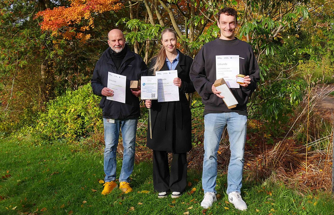 Drei Personen mit Urkunden im Botanischen Garten der HHU.