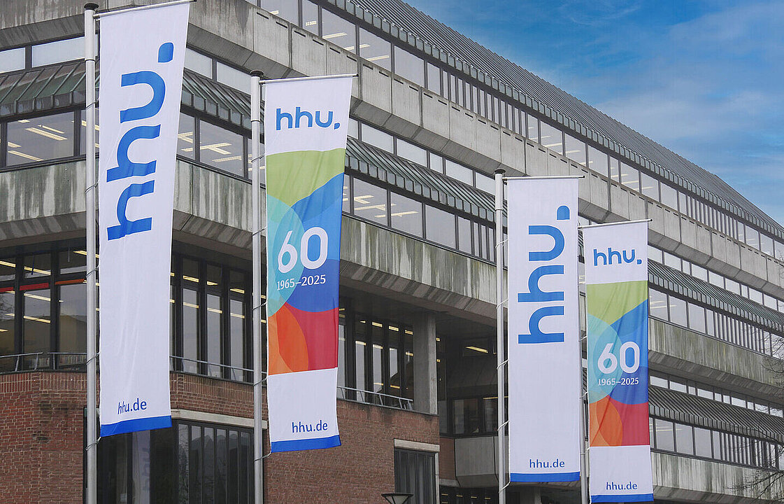 Bunte Fahnen, die auf den 60. Geburtstag der HHU hinweisen, vor dem Gebäude der ULB.