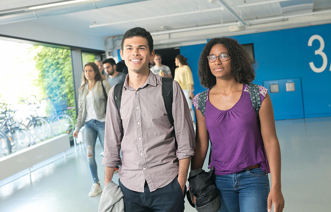 Zwei Personen laufen vor einer Gruppe von Menschen, die einen Hörsaal verlässt