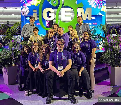 Gruppenbild des HHU-iGEM-Teams vor dem Logo des Wettwerbs.