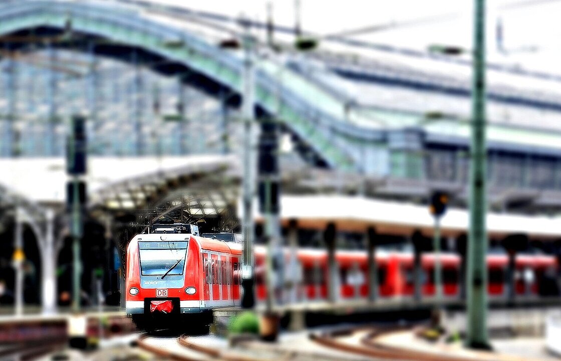 Im Hintergrund ein Bahnhof und davor ein ausfahrender Zug